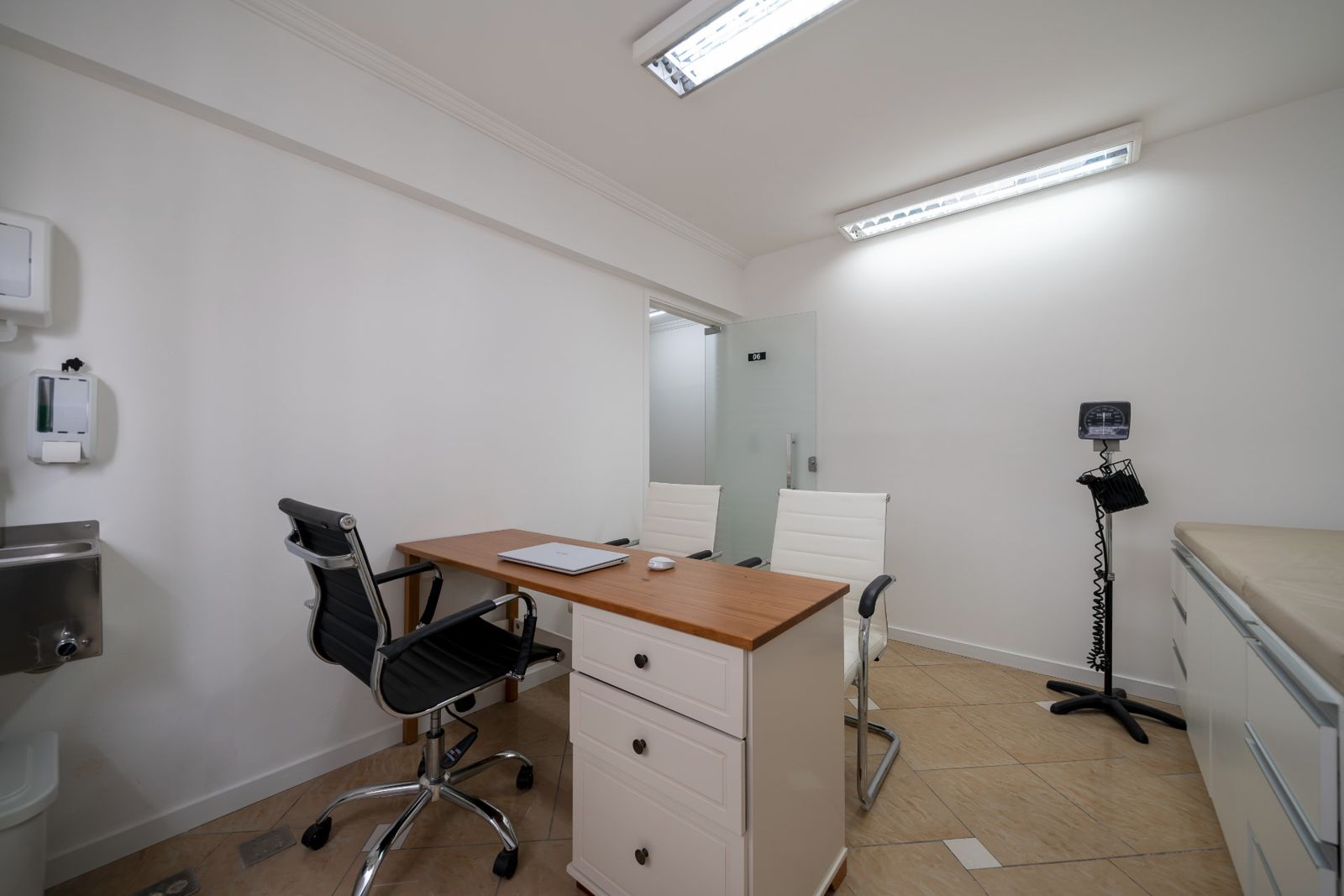 Consultório 06 com mesa de atendimento, pia e esfigmomanômetro